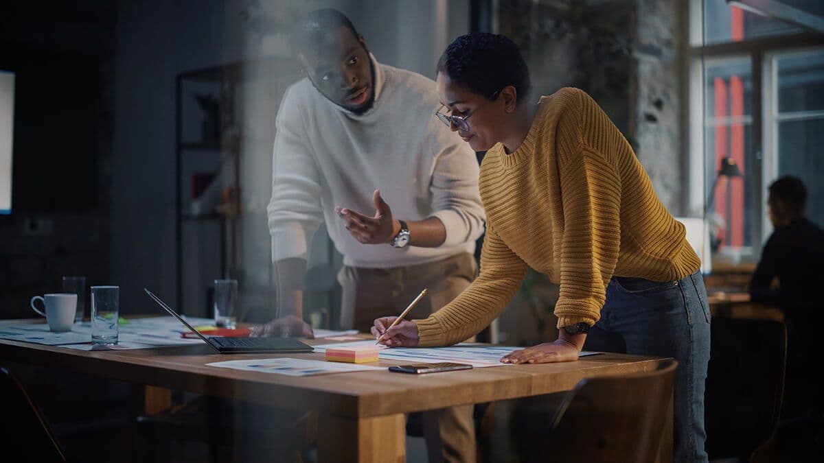 Two colleagues standing at a desk in a modern office discussing professional goals