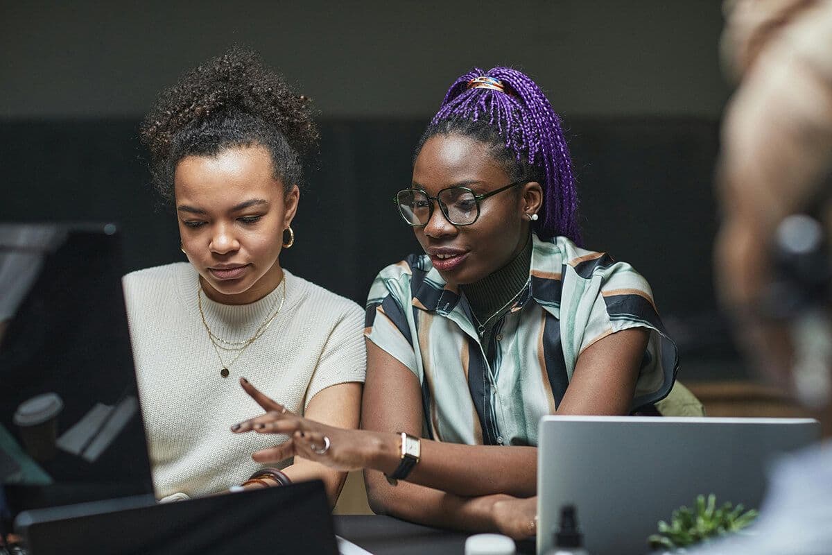 Two women sitting in an office looking at a desktop computer as part of a team mentoring session